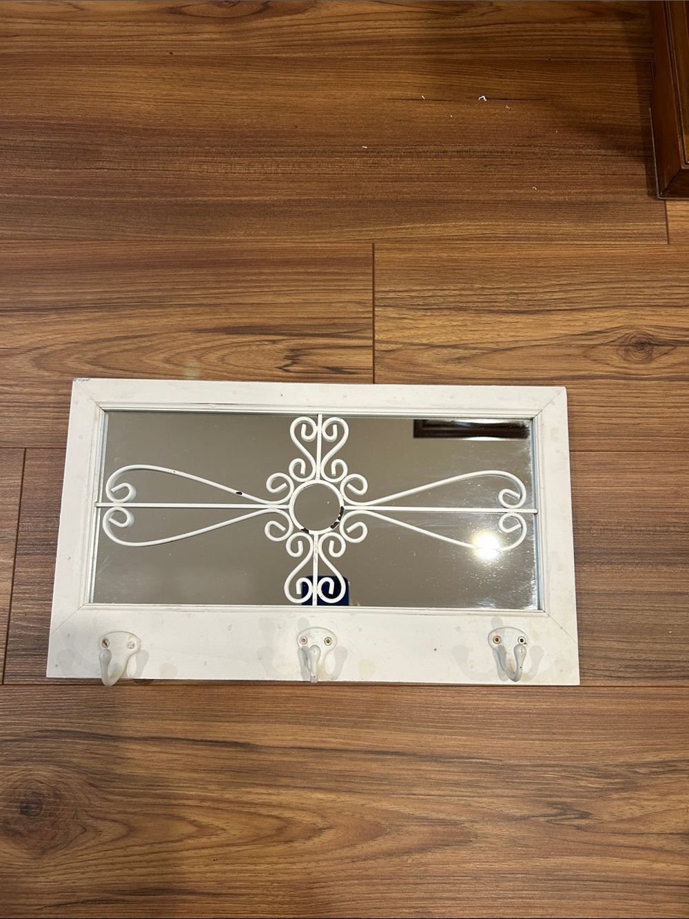 White distressed mirror with three hooks.